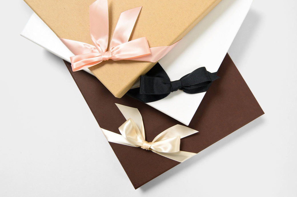 Three Boutique Boxes, one kraft with pink ribbon, one pebble with black ribbon, and one coffee with cream ribbon.