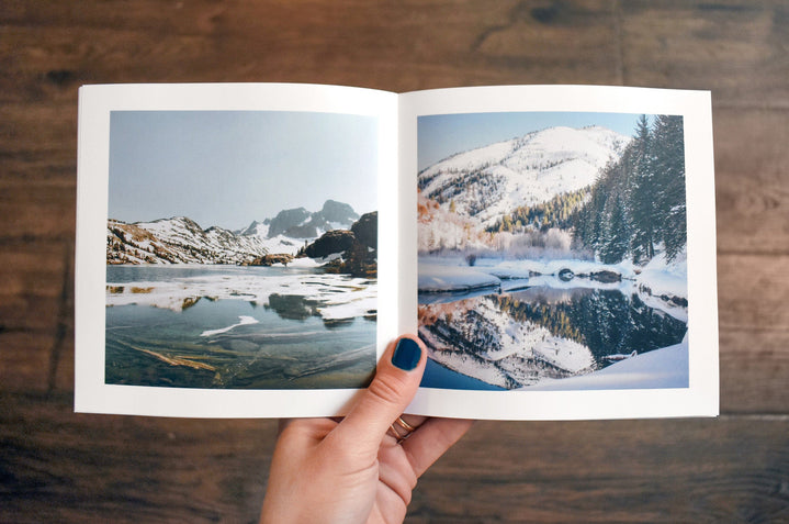 A hand holding a Buzz Book open to a spread featuring wintery landscape photos. 