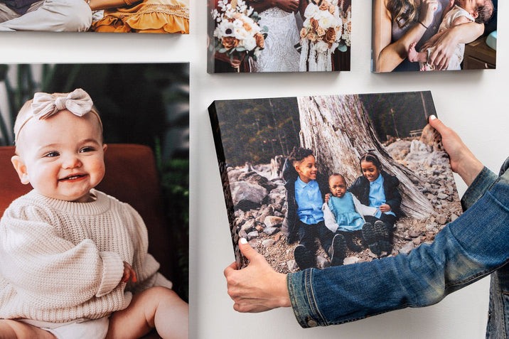 Gallery wall of Premium Canvases, one canvas featuring a photo of three children is being hung on the wall.