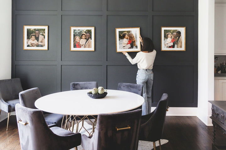 Dining room scene of a woman in front of a series of four 24x24" Gold, Thin Safari Framed Prints on a blue wall. 