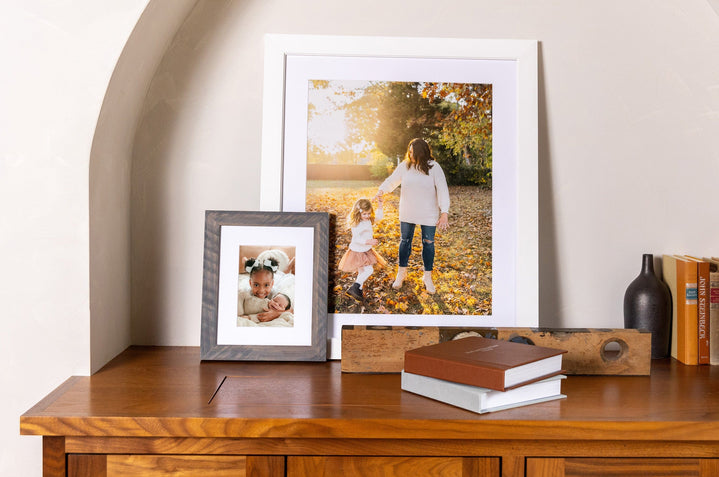 A 20x24" and an 8x10" Wood Frame styled on a sideboard with books. The Framed Prints featured images of young girls and a mother. 