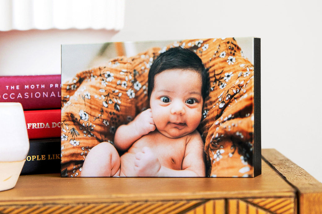 5x7" Gallery Block styled on a bedside table featuring a photo of a baby on an orange blanket. 