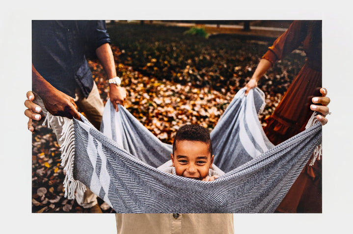 Woman holding a 20x30" Photo Print featuring a picture of a child being swung in a blanket over a bed of leaves. 