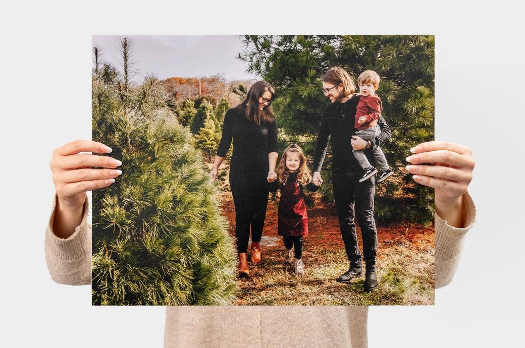 Woman holding up a 16x20" Landscape Lustre Photo Print with a picture of a family in a Christmas tree farm.