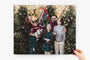 11x14" Photo Print being held by a woman's hand. The Photo Print features a family surrounded by pine trees being snowed on. 