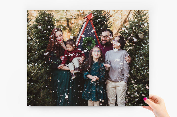 11x14" Photo Print being held by a woman's hand. The Photo Print features a family surrounded by pine trees being snowed on. 