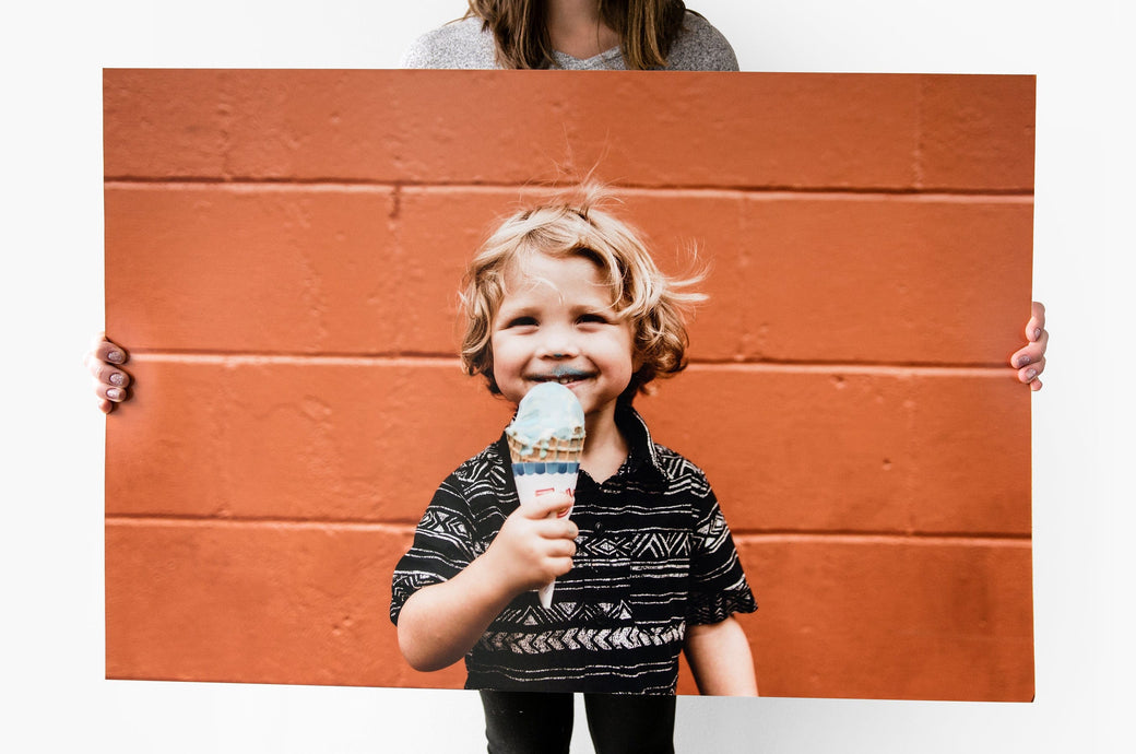 24x36" Photo Print being held up by a woman. The Photo Print features a picture of a young child eating ice cream in front of an orange wall - Nations Photo Lab