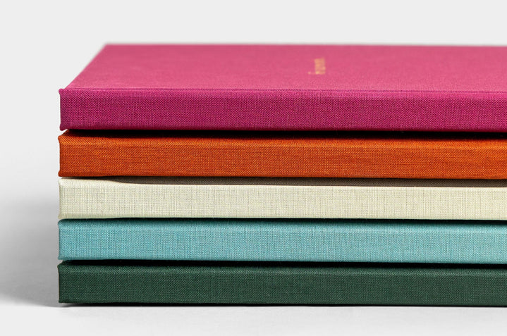 Stack of five Photo Books, featured covers are Mulberry Linen, Rust Linen, Pistachio Linen, Seamist Linen, Evergreen Linen