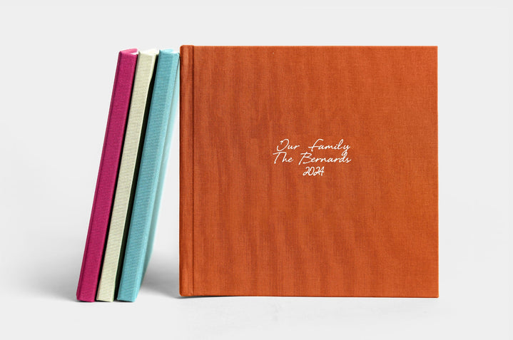 Four 8x8" Lay Flat Photo Books, covers featured are Mulberry Linen, Pistachio Linen, Seamist Linen, and Rust Linen. The Rust Linen book has white embossing in Eye Catching. 