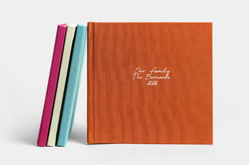 Four 8x8" Lay Flat Photo Books, covers featured are Mulberry Linen, Pistachio Linen, Seamist Linen, and Rust Linen. The Rust Linen book has white embossing in Eye Catching. 