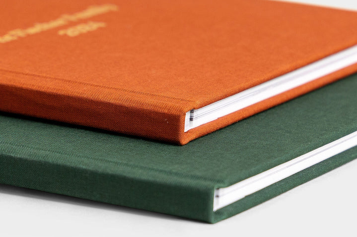 Two Lay Flat Photo Books stacked together, featured covers are Rust Linen and Evergreen Linen